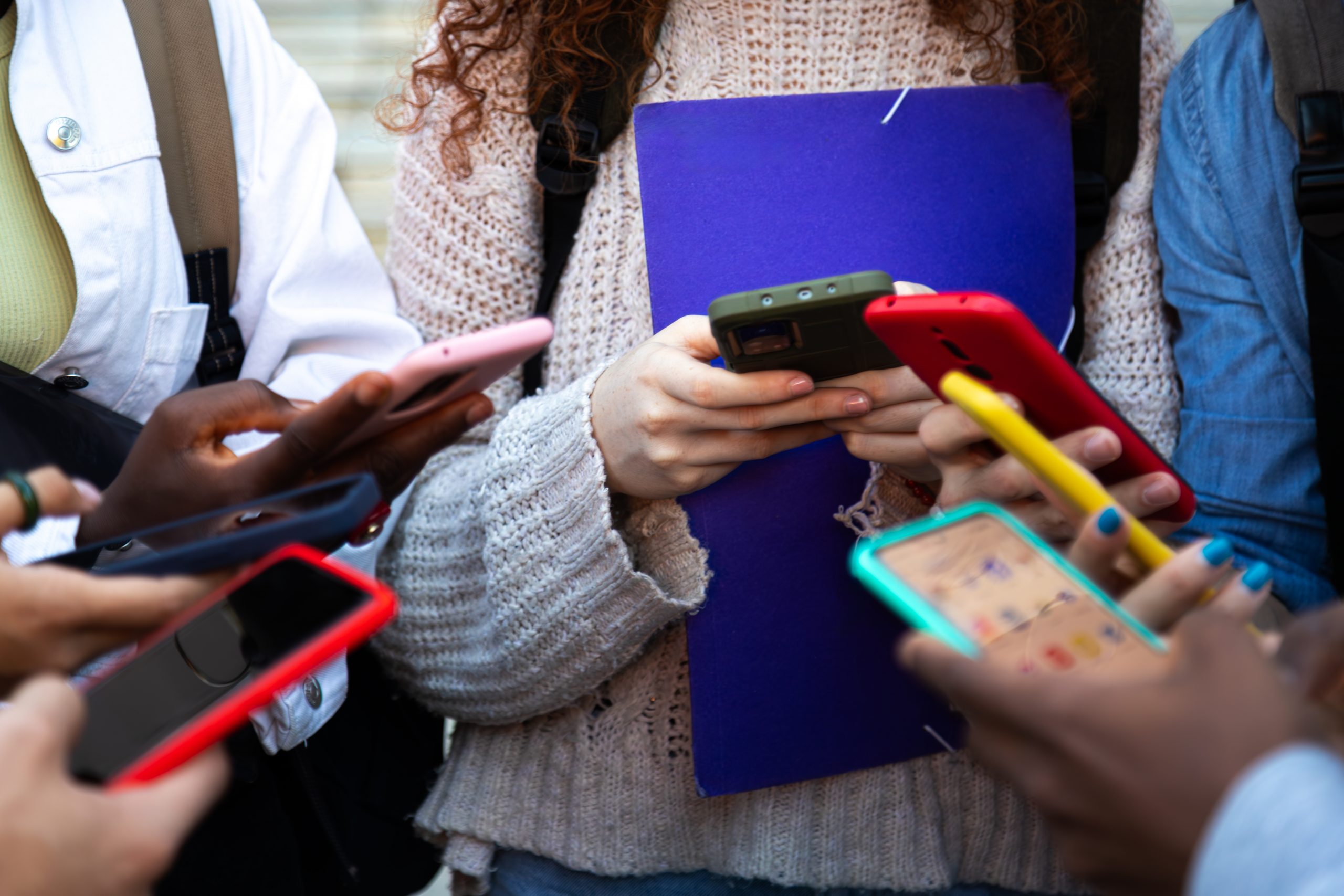 A group of young people stand huddled in a circle using smartphones. 