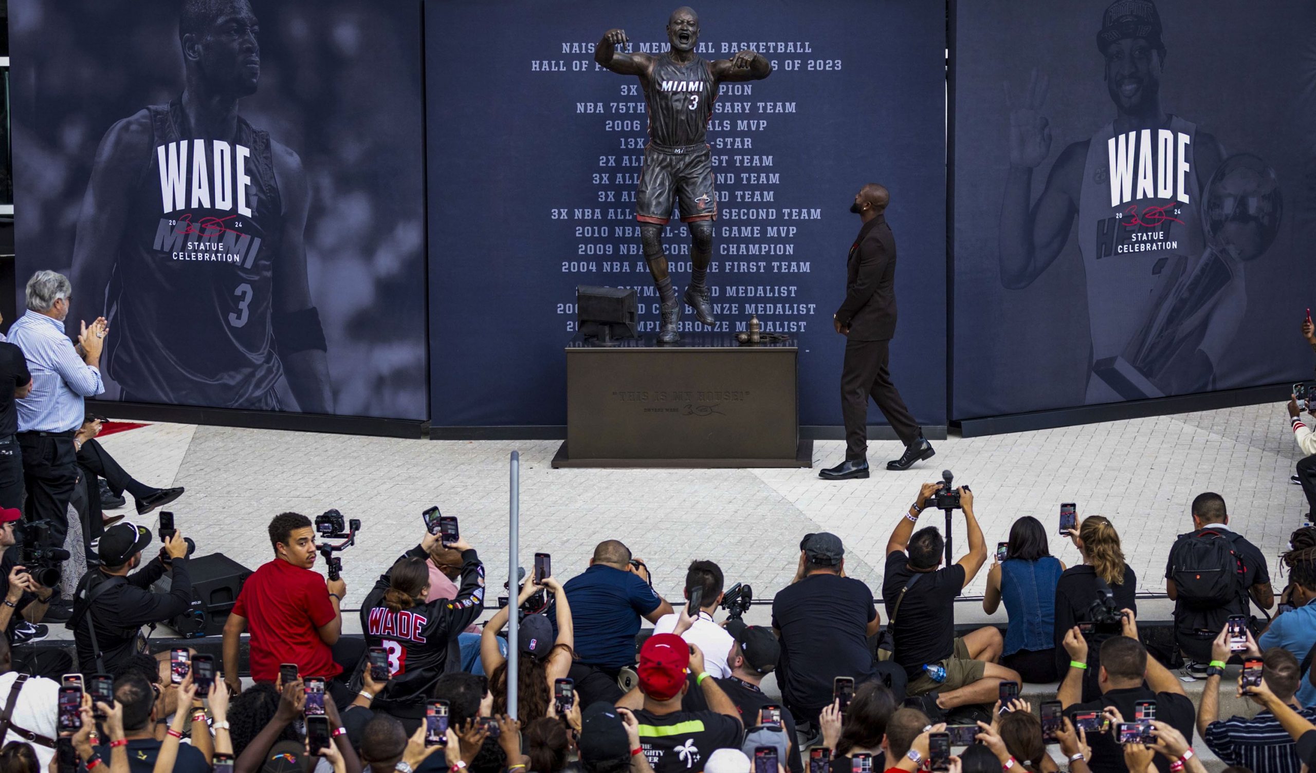 dwyane wade walking in front of his statue in miami as a crowd looks on