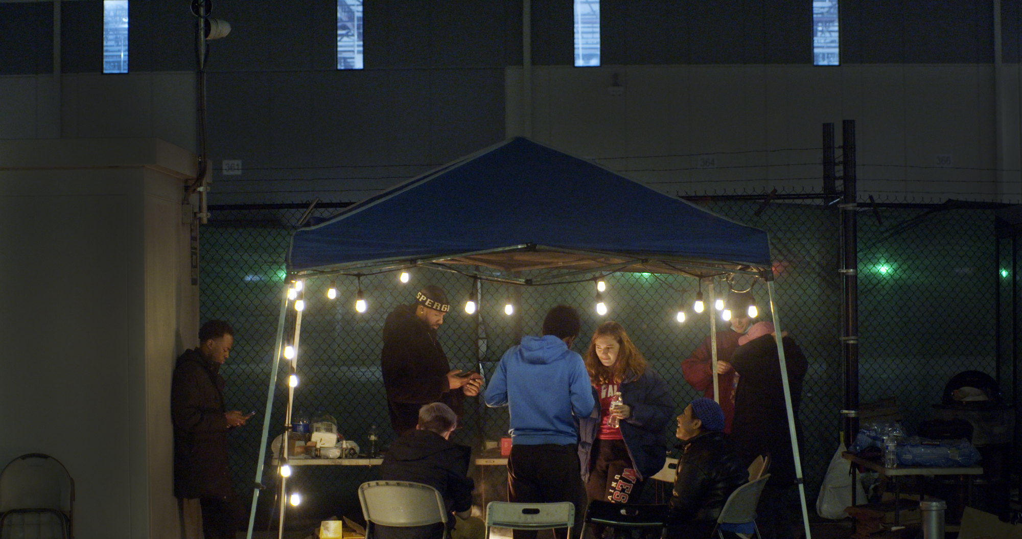 A group of organizers stand under a canopy lit by string lights.