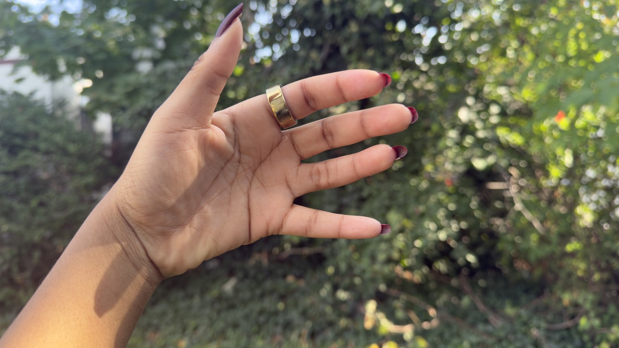 Oura Ring 4 gold variant on woman's finger surrounded by greenery