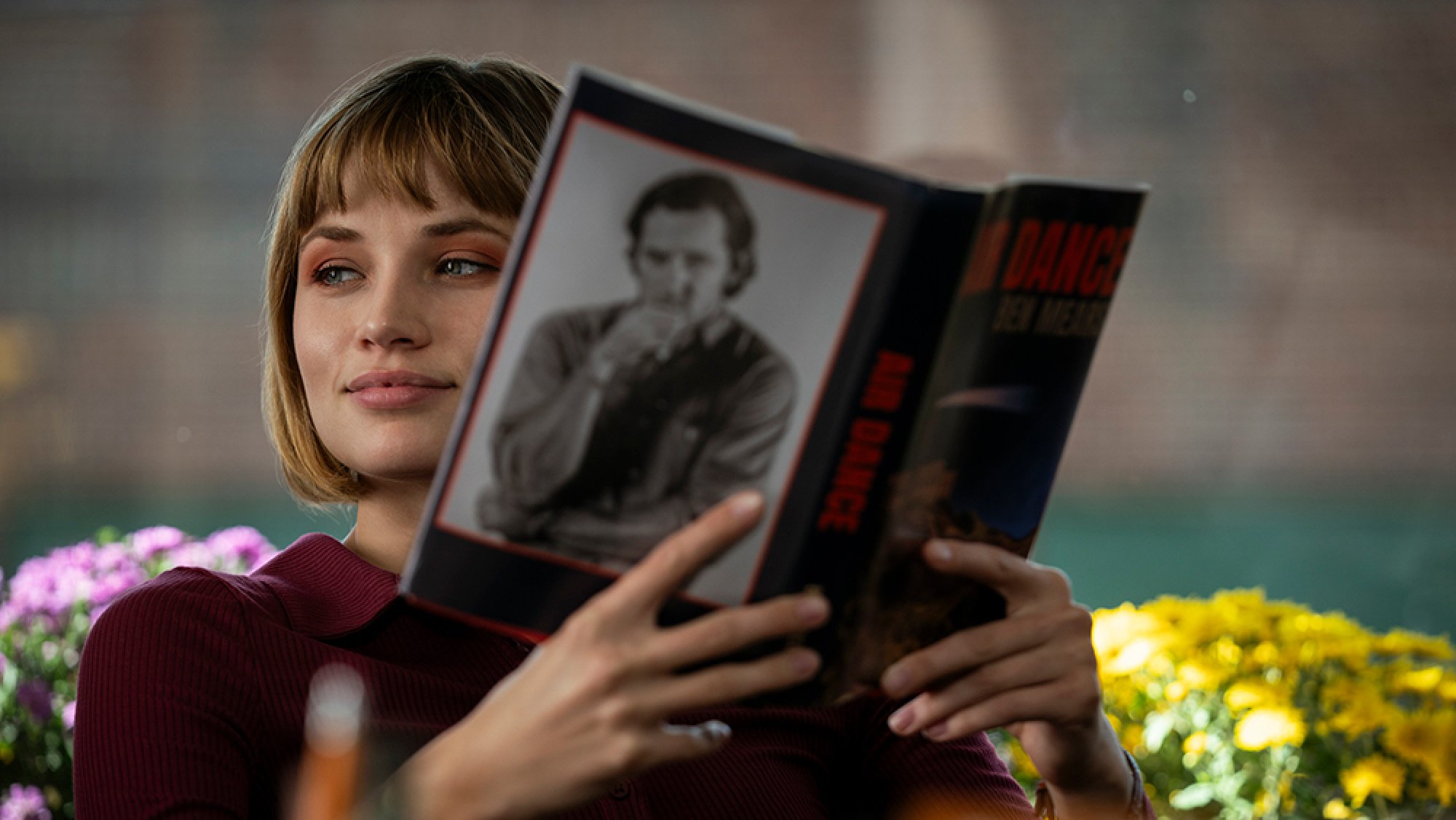 A woman sits in a chair by the window, reading a book.