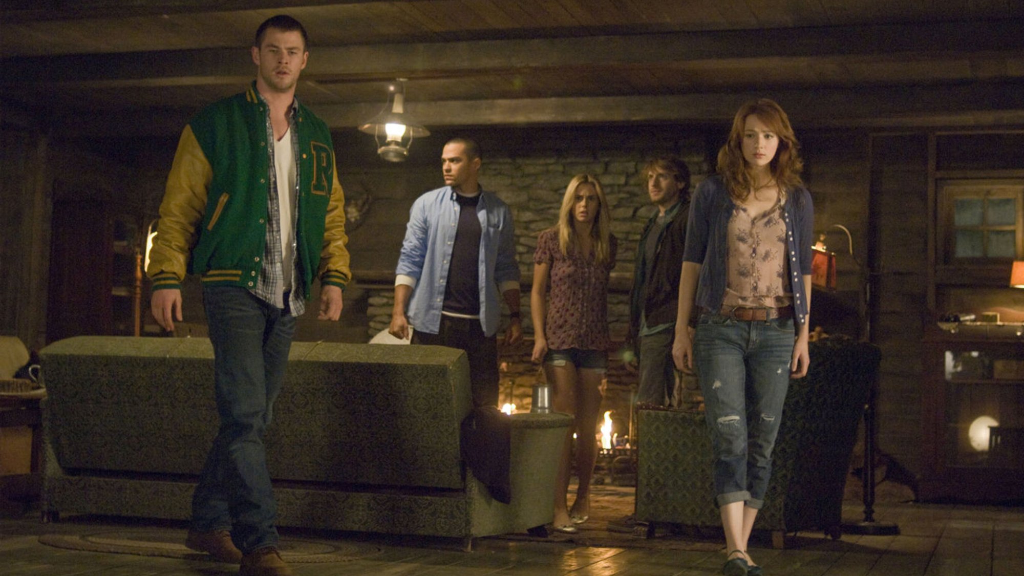 A group of young people stand around a cabin looking afraid.