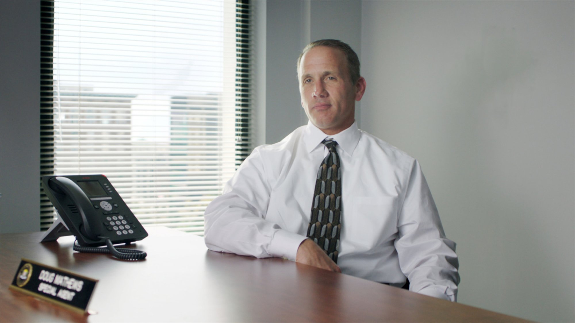 A man in a suit sits at a conference table. 