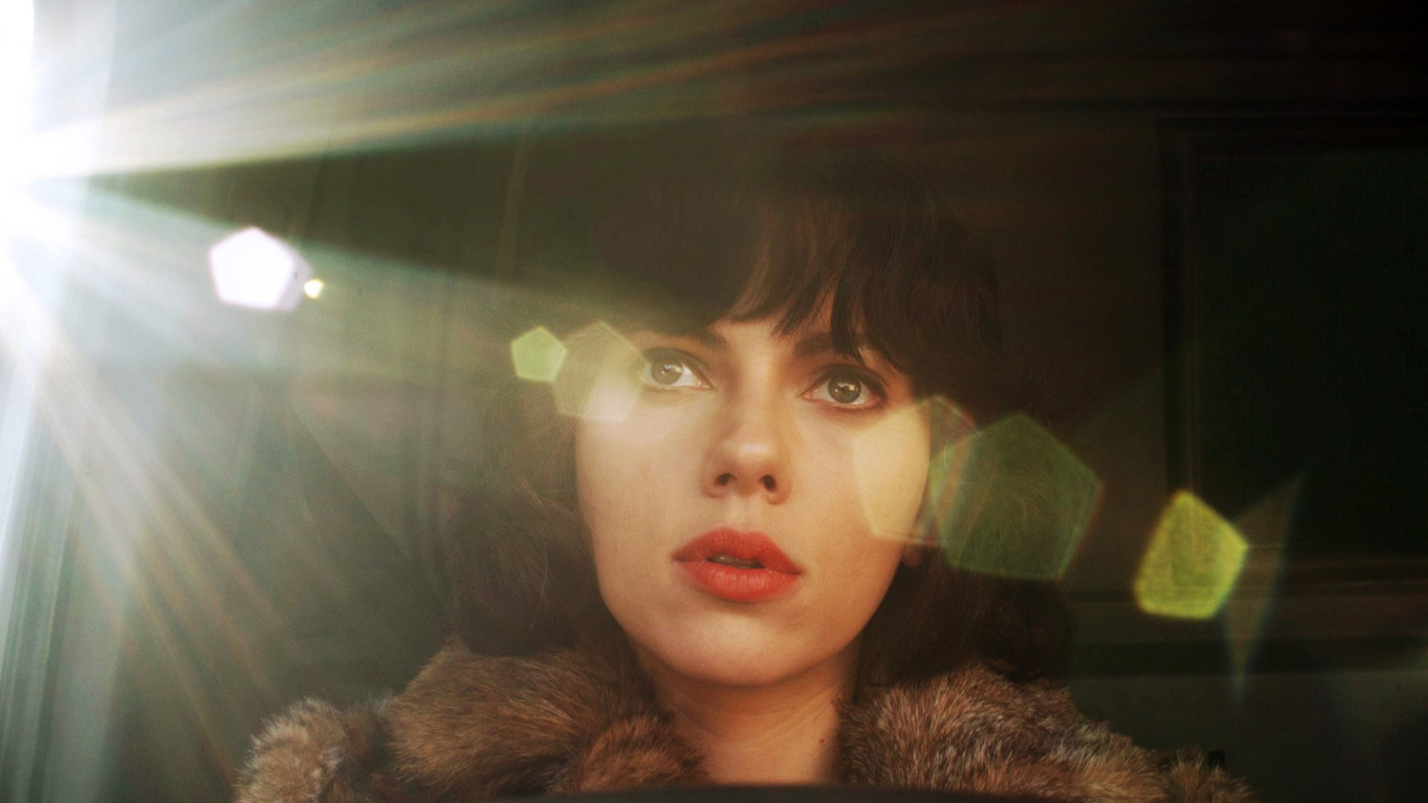 Scarlett Johansson looks out a car window as a sun flare comes across the frame.