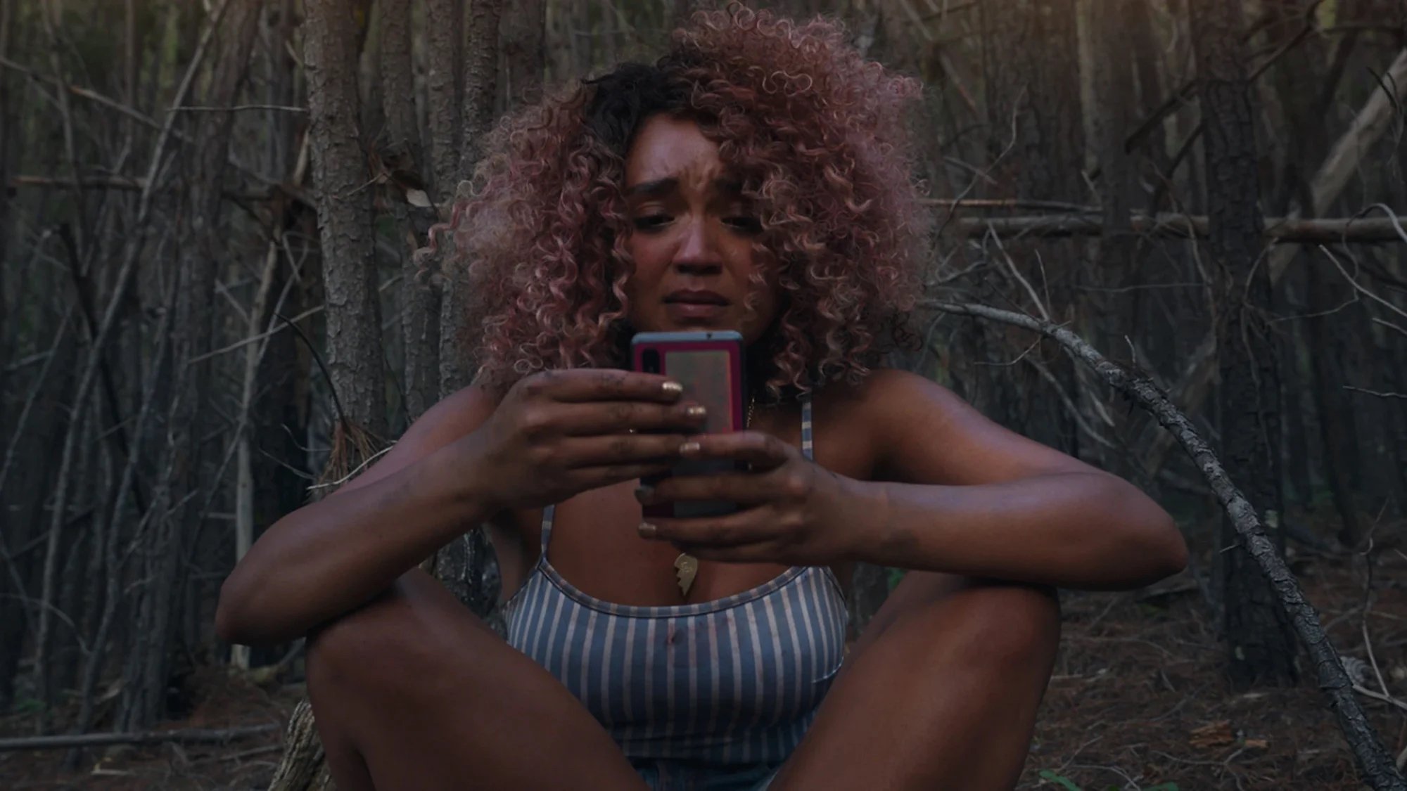 Aisha Dee sits in distress looking at her phone in the film "Sissy."