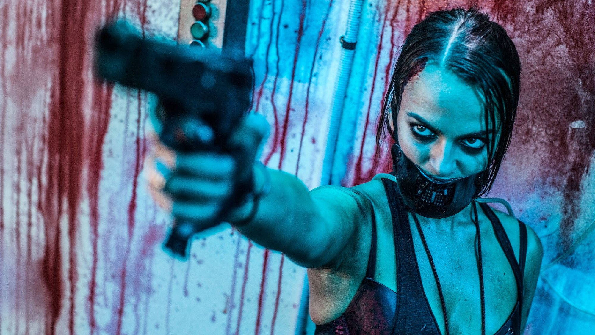 Bianca Bradey stands holding a gun with a mouth covering in a bloody room in "Wyrmwood: Road of the Dead."