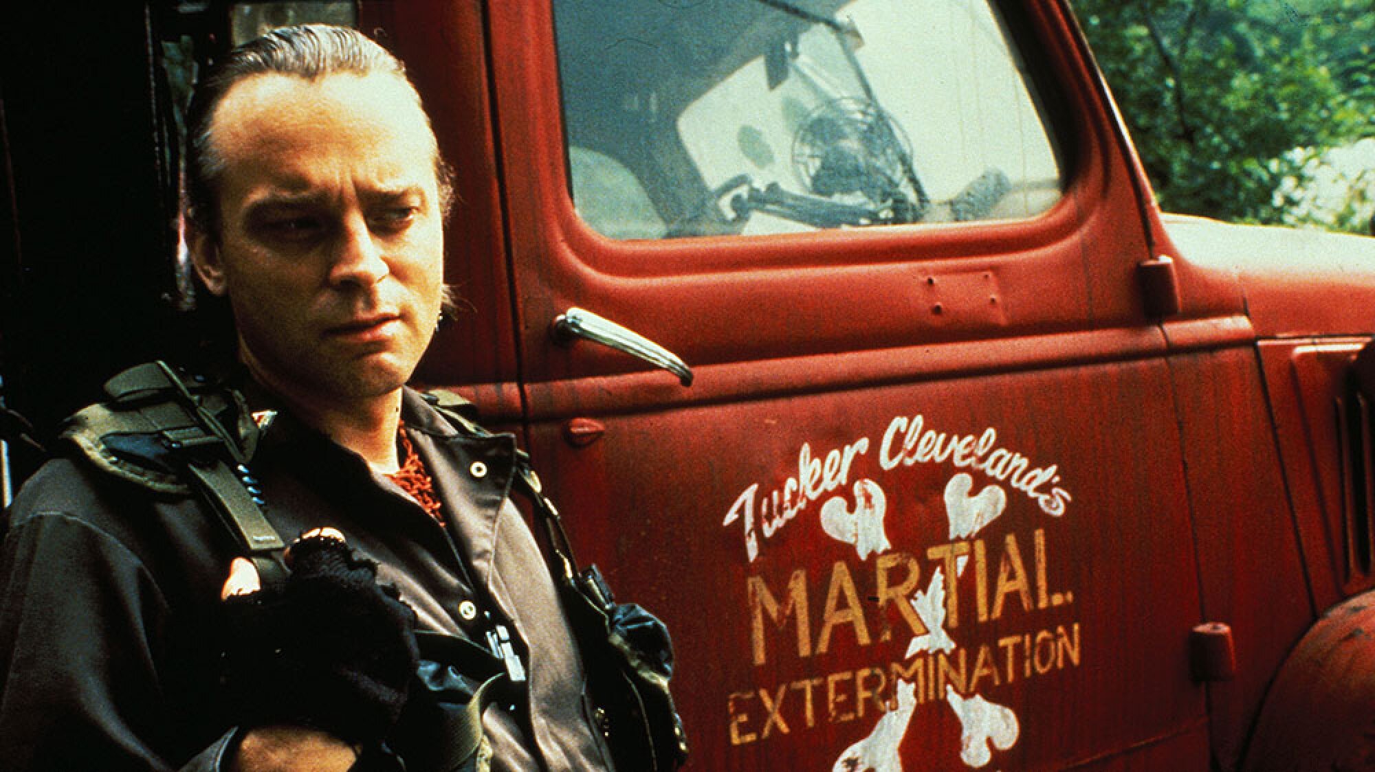 A man leans on a red pickup truck.