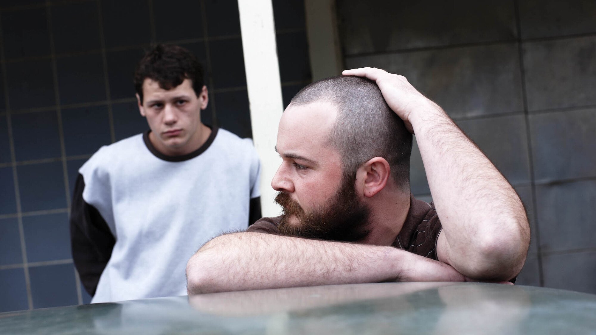 Two men stand looking grim beside a car in the film "Snowtown".