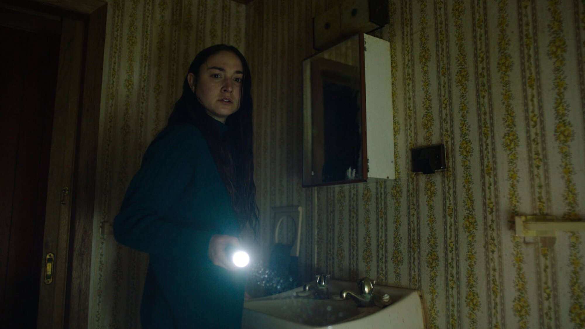 Jordan Cowan shines a torch into a dark bathroom in the film "You'll Never Find Me."