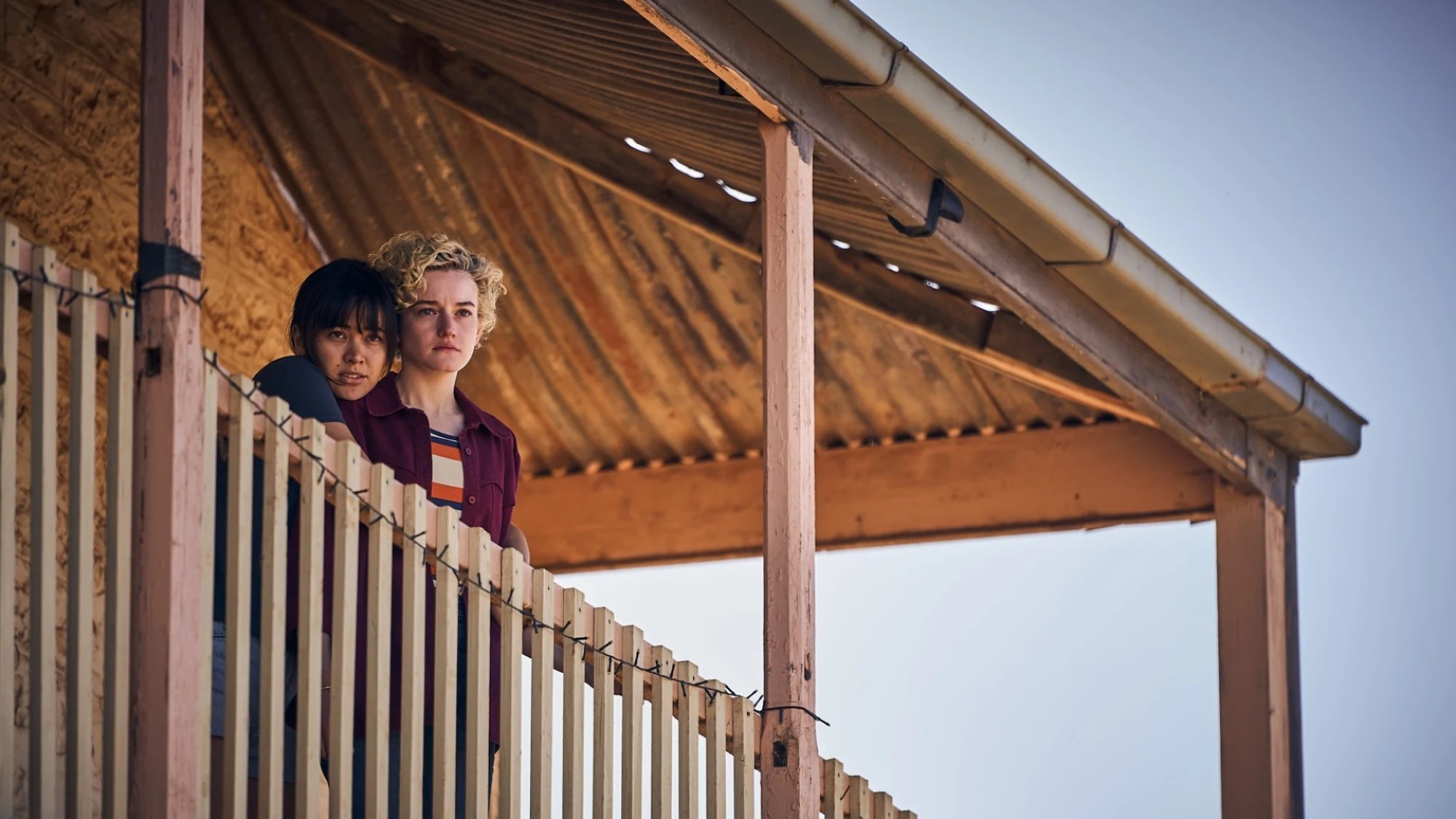 Jessica Henwick and Julia Garner stand on a pub verandah looking worried in the film "The Royal Hotel."