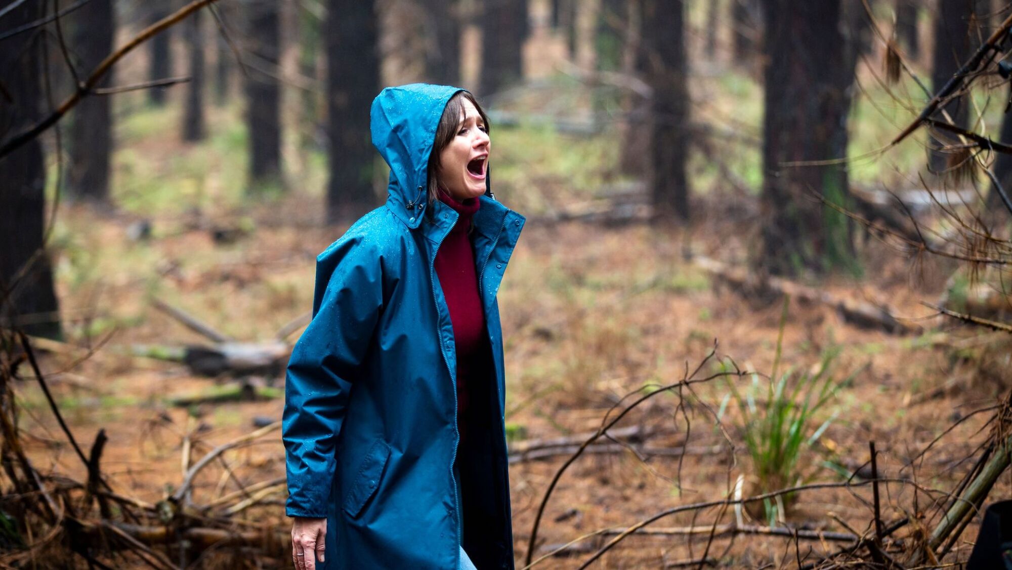 Emily Mortimer stands in a forest wearing a blue jacket screaming in the film "Relic."