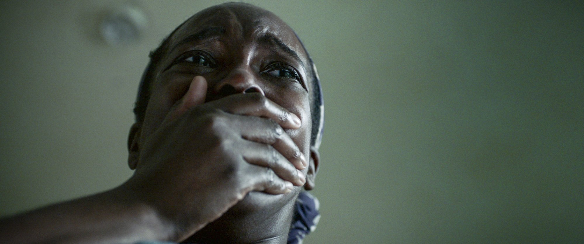 A woman has her hand cupped over her mouth in terror. 