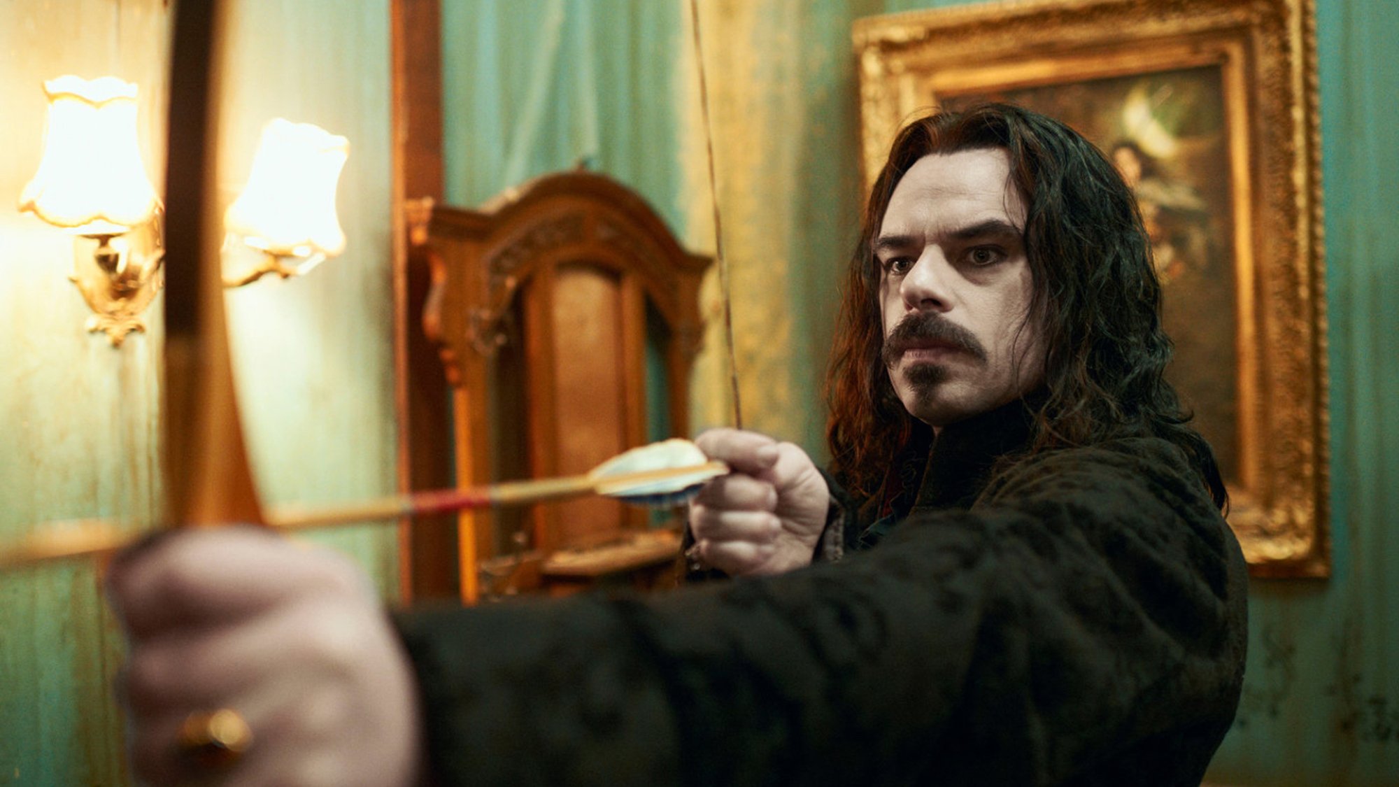 Jemaine Clement holds a bow and arrow in an old fashioned room in the TV show "What We We Do in the Shadows."