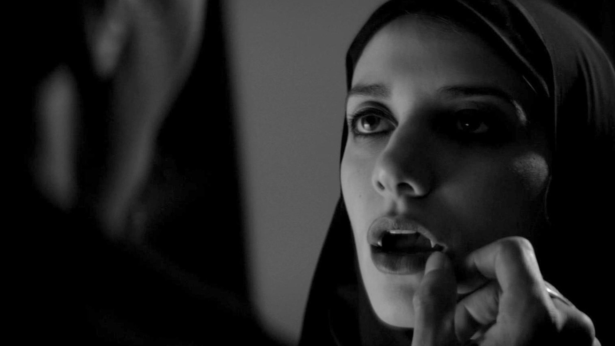 A woman shows she has fanged teeth in a moody film still from "A Girl Walks Home Alone At Night."