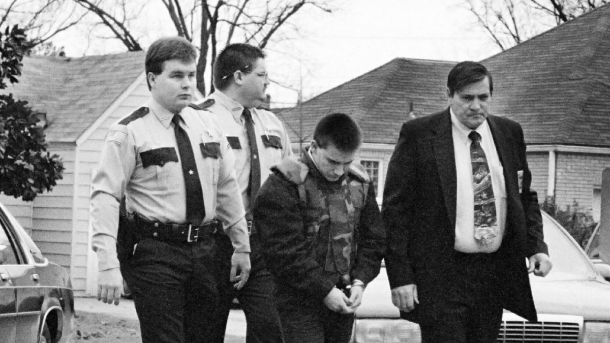 A handcuffed boy is escorted by police