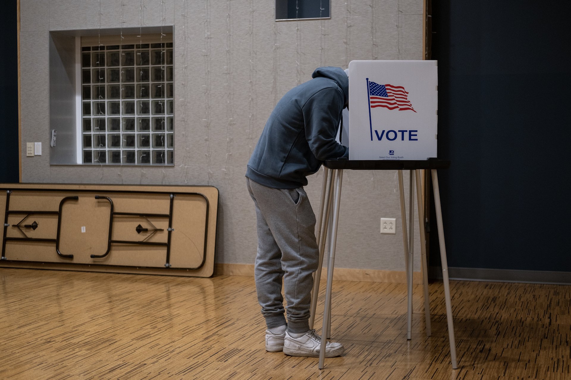 A voter leans over their ballot in a voting booth.