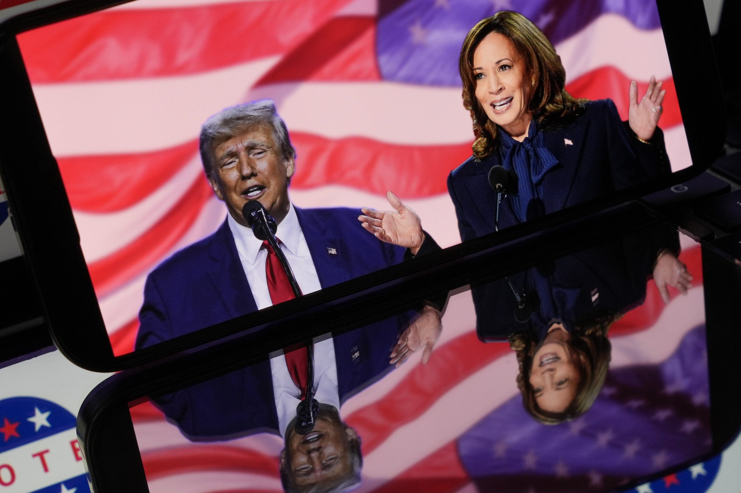 A photo of Harris and Trump on a phone screen with American flags and imagery reflected around them.