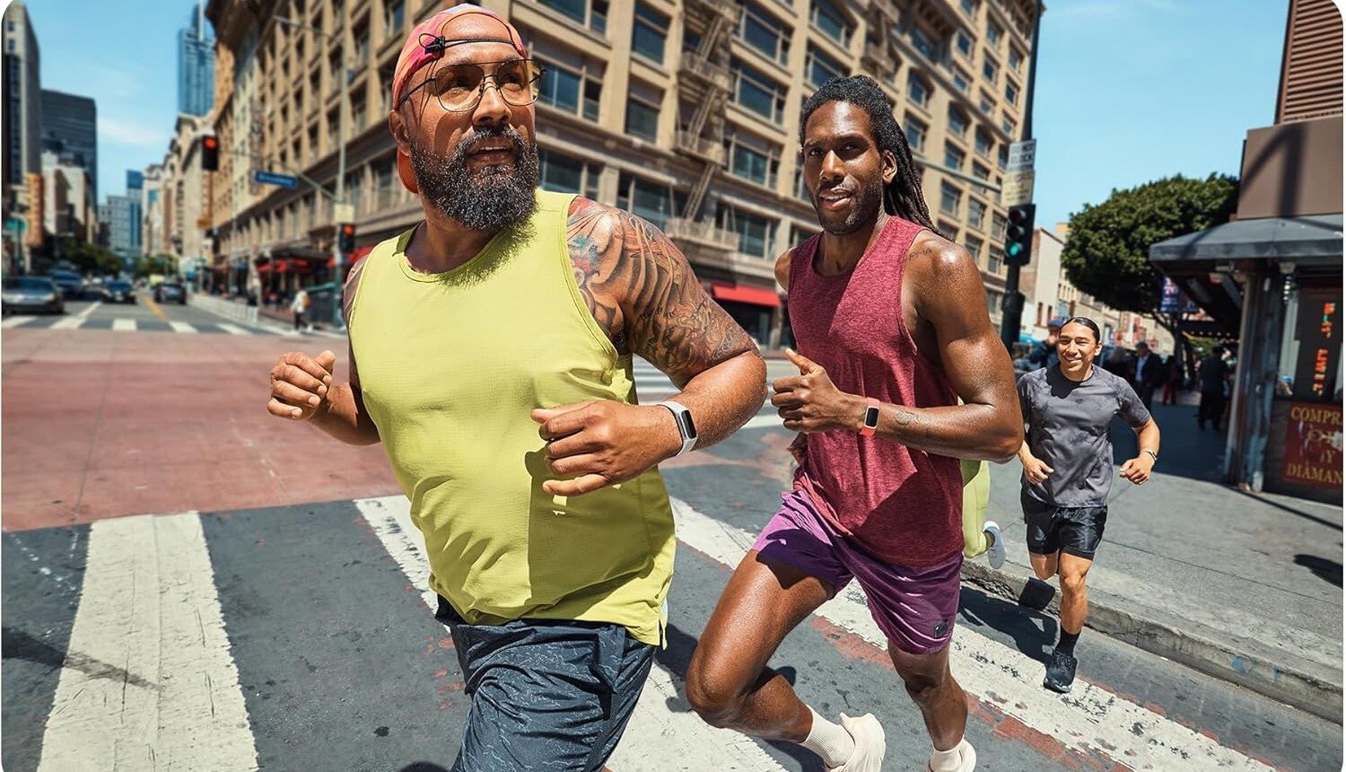 three people run through an intersection in a busy metropolitan area while wearing fitbit watches